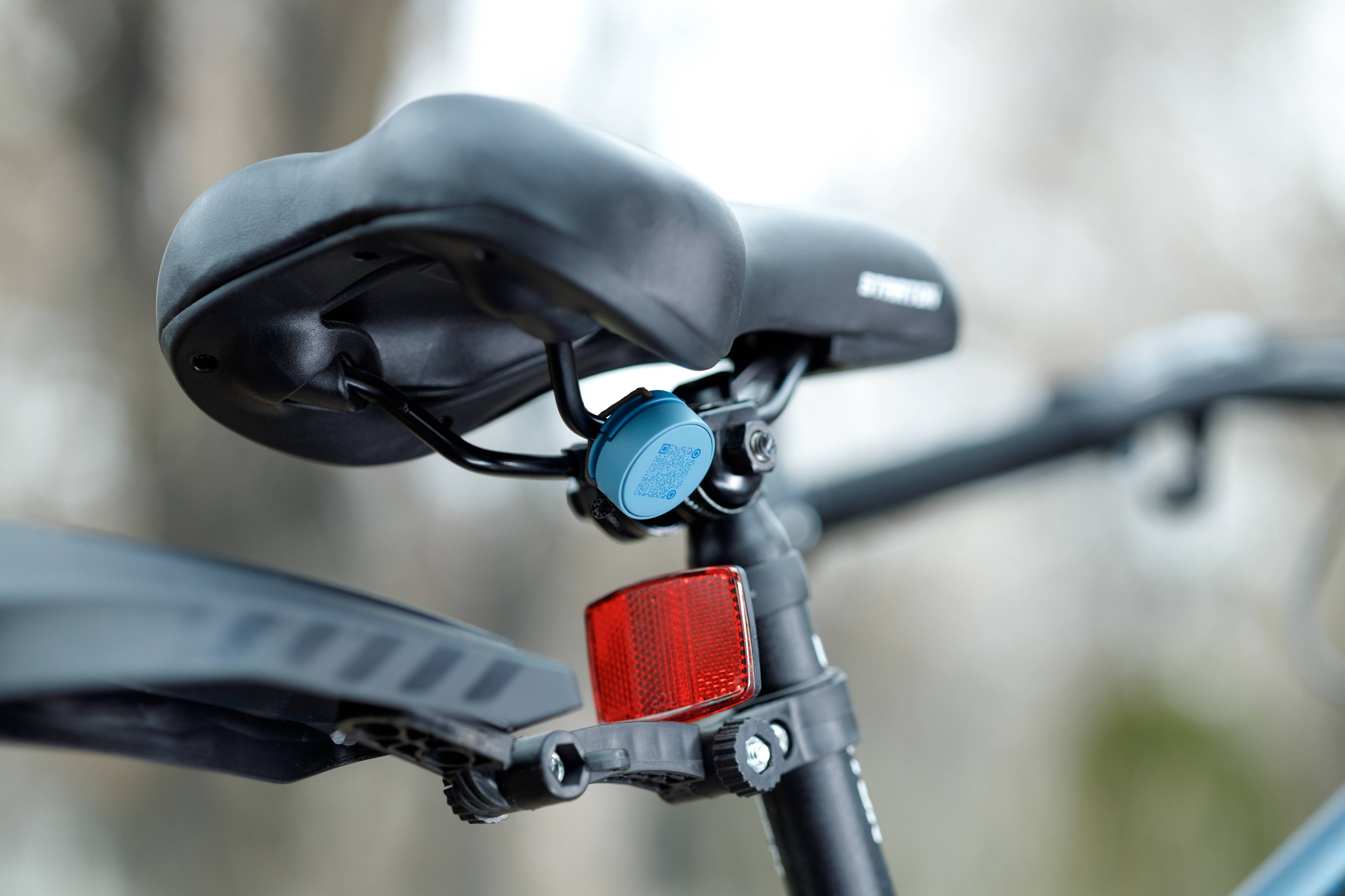 Blue Roam Smart Tracker mounted under a black bicycle seat saddle with red tail light showing best GPS tracker for bike security and anti-theft