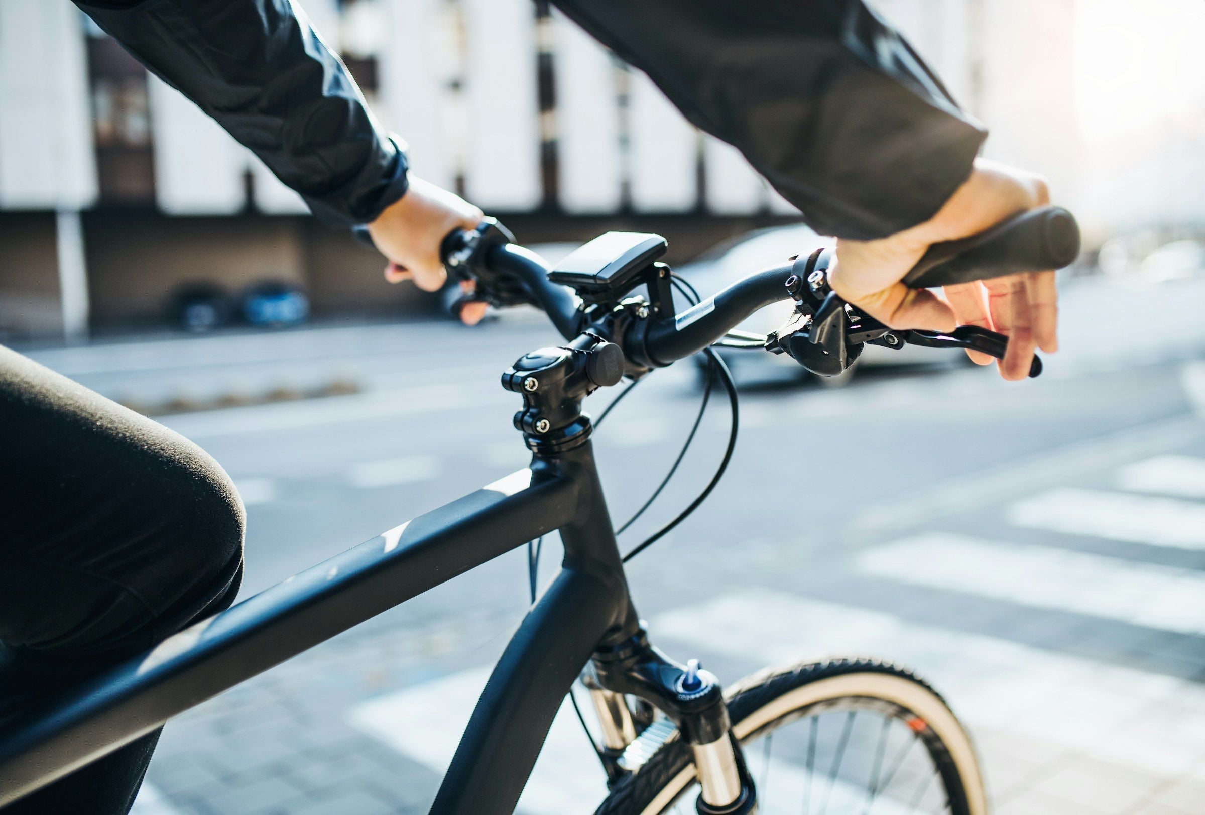 Person riding a black bicycle on a city street close up view of handlebars showing back to school tracking with Roam Smart Tracker